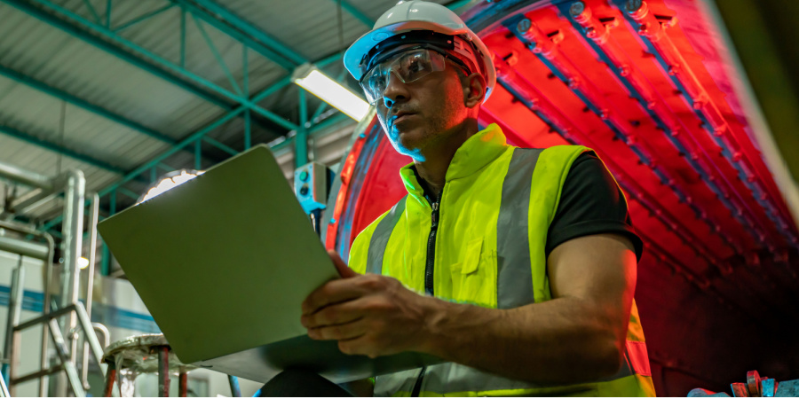 heavy equipment manufacturing employee wearing a hard hat and using a laptop | Finding the Right LMS as a Heavy Equipment Manufacturer
